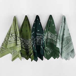 May include: Five green bandanas with paisley patterns hang against a white wall. The bandanas vary in shades of green, from light to dark, and are folded to display their designs. Each bandana has a unique paisley pattern.