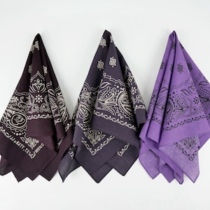 Op de afbeelding: Drie bandana's met paisley-patronen. Eén is paars, één is donkerpaars en één is zwart. De zwarte bandana heeft de tekst "J.W. HATY. TX. AROOSE" erop gedrukt.
