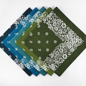 May include: A collection of six square bandanas in shades of blue and green, arranged in a diagonal line. Each bandana features a white floral pattern, with some having a border design and others with scattered floral motifs. The bandanas are made of a soft fabric.