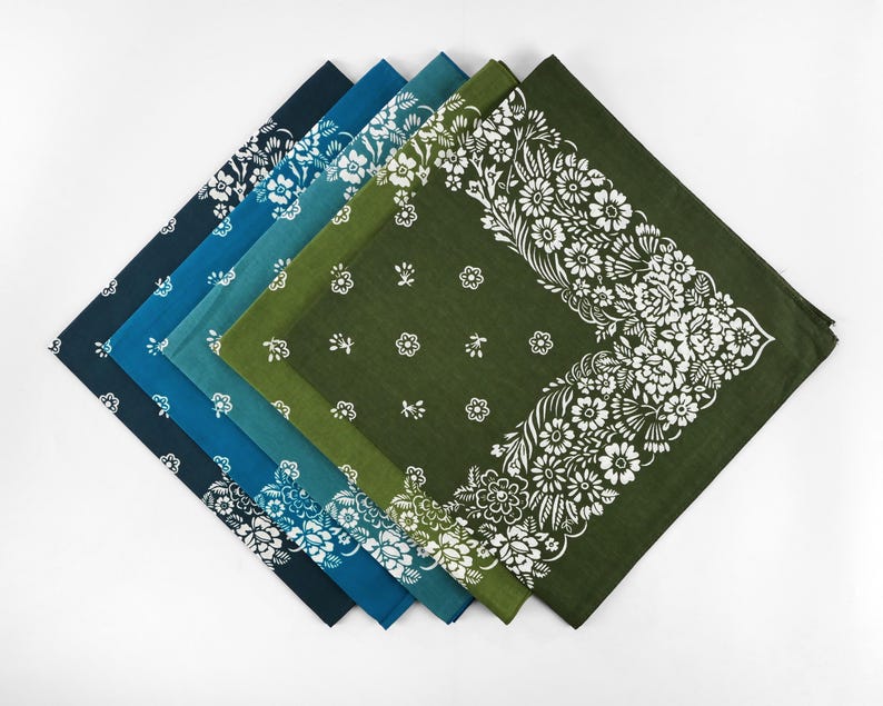 May include: A collection of six square bandanas in shades of blue and green, arranged in a diagonal line. Each bandana features a white floral pattern, with some having a border design and others with scattered floral motifs. The bandanas are made of a soft fabric.