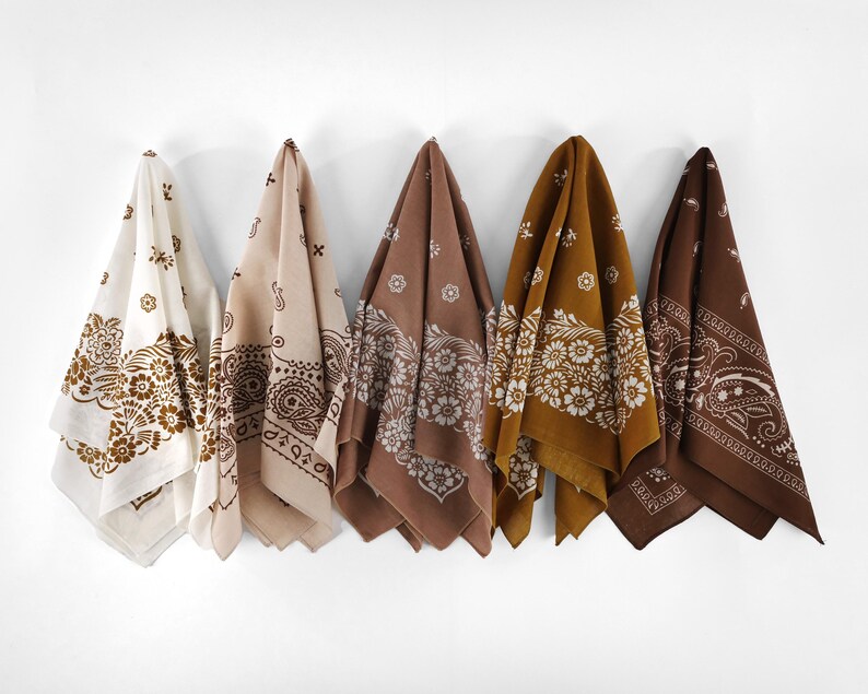 May include: Five bandanas in varying shades of brown and cream hang against a white wall. Each bandana features a different floral or paisley pattern. The bandanas are made of a soft fabric.