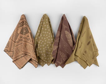 Könnte beinhalten: Vier dekorative Küchentücher mit verschiedenen Mustern hängen an einer weißen Wand. Die Muster umfassen geometrische Formen, florale Designs und stilisierte Fische. Die Farben sind Beige, Olivgrün und Braun.