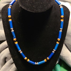 May include: A blue, orange, black, and silver beaded necklace on a black display stand.