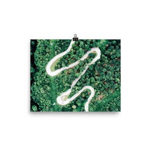 May include: An aerial view of a winding white road through a dense green forest. The road curves and twists through the trees, creating a unique and interesting pattern.