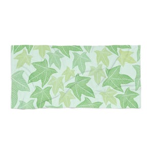 Puede incluir: Una toalla de playa rectangular con un patrón repetido de hojas de hiedra verdes y verde claro sobre un fondo azul claro. Las hojas tienen patrones de venas detallados.
