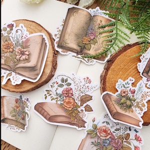 May include: Five vintage-style book stickers with floral illustrations. Each sticker features an open book with a bouquet of flowers in the center. The books are brown with gold accents and the flowers are in shades of pink, purple, and white.