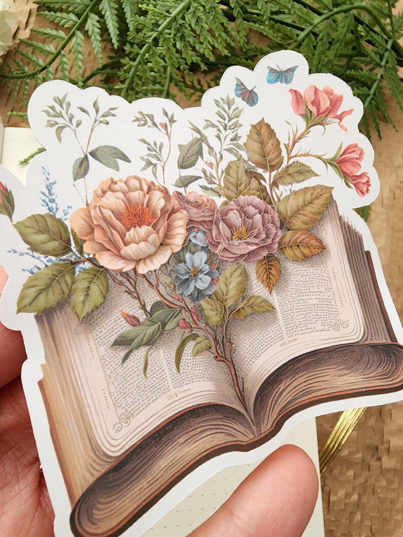 May include: A vintage style sticker featuring an open book with a bouquet of flowers, including roses, blue flowers, and green leaves. A blue butterfly is flying above the flowers. The book has text on the pages and a brown cover.