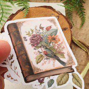 May include: A vintage book sticker with a floral design and a bird perched on a branch. The book is brown with gold accents and the flowers are pink, orange, and yellow.