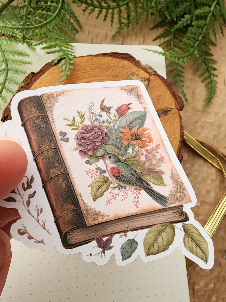 May include: A vintage book sticker with a floral design and a bird perched on a branch. The book is brown with gold accents and the flowers are pink, orange, and yellow.