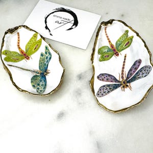 Handmade dragonfly oyster shell trinket dish with hand-gilded gold leaf edges and glossy resin finish, created from sustainably sourced Dorset shells. Unique coastal jewellery holder and ring dish, ideal as a vanity tray, trinket tray or decorative keepsake. Nature inspired home decor gift for birthdays, weddings, anniversaries, housewarmings and Mother’s Day. One of a kind artisan shell dish, beautifully presented in a gift box.