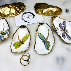 Handmade dragonfly oyster shell trinket dish with hand-gilded gold leaf edges and glossy resin finish, created from sustainably sourced Dorset shells. Unique coastal jewellery holder and ring dish, ideal as a vanity tray, trinket tray or decorative keepsake. Nature inspired home decor gift for birthdays, weddings, anniversaries, housewarmings and Mother’s Day. One of a kind artisan shell dish, beautifully presented in a gift box.