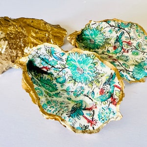 May include: Three decorative oyster shells with gold edges. The inside of the shells are lined with a floral pattern in shades of blue, green, and white.