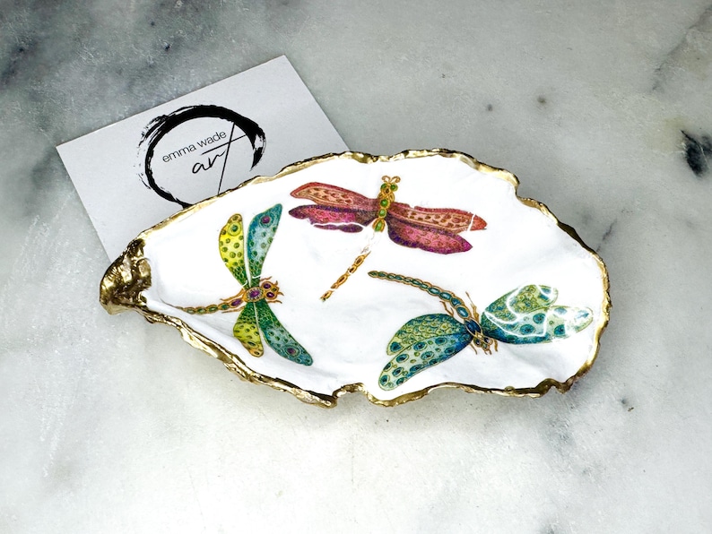 Handmade dragonfly oyster shell trinket dish with hand-gilded gold leaf edges and glossy resin finish, created from sustainably sourced Dorset shells. Unique coastal jewellery holder and ring dish, ideal as a vanity tray, trinket tray or decorative keepsake. Nature inspired home decor gift for birthdays, weddings, anniversaries, housewarmings and Mother’s Day. One of a kind artisan shell dish, beautifully presented in a gift box.
