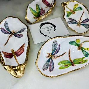Handmade dragonfly oyster shell trinket dish with hand-gilded gold leaf edges and glossy resin finish, created from sustainably sourced Dorset shells. Unique coastal jewellery holder and ring dish, ideal as a vanity tray, trinket tray or decorative keepsake. Nature inspired home decor gift for birthdays, weddings, anniversaries, housewarmings and Mother’s Day. One of a kind artisan shell dish, beautifully presented in a gift box.
