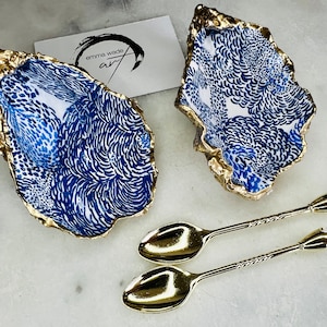 May include: Two gold oyster shell dishes with a blue and white floral pattern and two gold spoons with clear crystal handles.