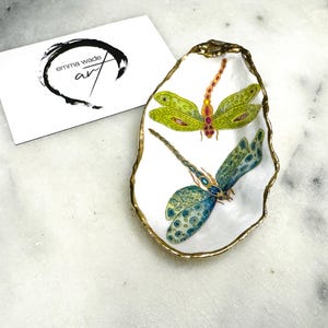 Handmade dragonfly oyster shell trinket dish with hand-gilded gold leaf edges and glossy resin finish, created from sustainably sourced Dorset shells. Unique coastal jewellery holder and ring dish, ideal as a vanity tray, trinket tray or decorative keepsake. Nature inspired home decor gift for birthdays, weddings, anniversaries, housewarmings and Mother’s Day. One of a kind artisan shell dish, beautifully presented in a gift box.