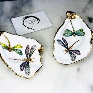 Handmade dragonfly oyster shell trinket dish with hand-gilded gold leaf edges and glossy resin finish, created from sustainably sourced Dorset shells. Unique coastal jewellery holder and ring dish, ideal as a vanity tray, trinket tray or decorative keepsake. Nature inspired home decor gift for birthdays, weddings, anniversaries, housewarmings and Mother’s Day. One of a kind artisan shell dish, beautifully presented in a gift box.