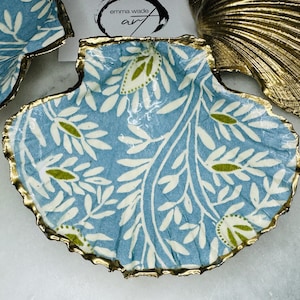 Op de afbeelding: Decoratieve schelpvormige schaal met een lichtblauwe achtergrond en een wit en groen bladerpatroon. De randen zijn afgewerkt met goud. De schaal maakt deel uit van een verzameling decoratieve items.