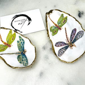 Handmade dragonfly oyster shell trinket dish with hand-gilded gold leaf edges and glossy resin finish, created from sustainably sourced Dorset shells. Unique coastal jewellery holder and ring dish, ideal as a vanity tray, trinket tray or decorative keepsake. Nature inspired home decor gift for birthdays, weddings, anniversaries, housewarmings and Mother’s Day. One of a kind artisan shell dish, beautifully presented in a gift box.
