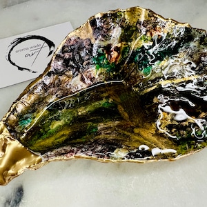 May include: A gold-painted, irregular-shaped dish with a green, black, and white abstract design. The dish is made of resin and has a glossy finish.