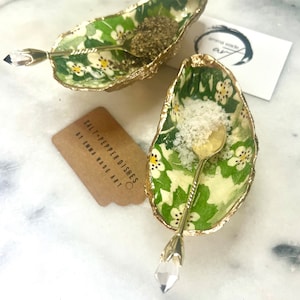 May include: Two gold oyster shell salt and pepper dishes with floral designs and crystal-tipped spoons. The dishes are filled with salt and pepper. The text on the tag reads "Salt-Pepper Dishes by Emma Wade Art".