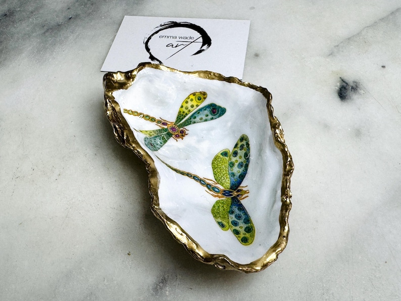 Handmade dragonfly oyster shell trinket dish with hand-gilded gold leaf edges and glossy resin finish, created from sustainably sourced Dorset shells. Unique coastal jewellery holder and ring dish, ideal as a vanity tray, trinket tray or decorative keepsake. Nature inspired home decor gift for birthdays, weddings, anniversaries, housewarmings and Mother’s Day. One of a kind artisan shell dish, beautifully presented in a gift box.