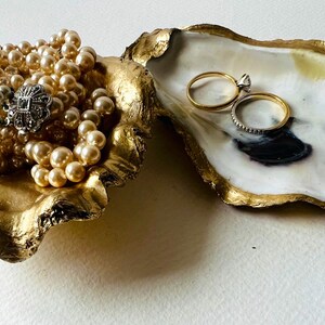 May include: A gold oyster shell ring dish with a pearl necklace inside and two gold rings in the other half of the shell.