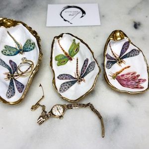 Handmade dragonfly oyster shell trinket dish with hand-gilded gold leaf edges and glossy resin finish, created from sustainably sourced Dorset shells. Unique coastal jewellery holder and ring dish, ideal as a vanity tray, trinket tray or decorative keepsake. Nature inspired home decor gift for birthdays, weddings, anniversaries, housewarmings and Mother’s Day. One of a kind artisan shell dish, beautifully presented in a gift box.