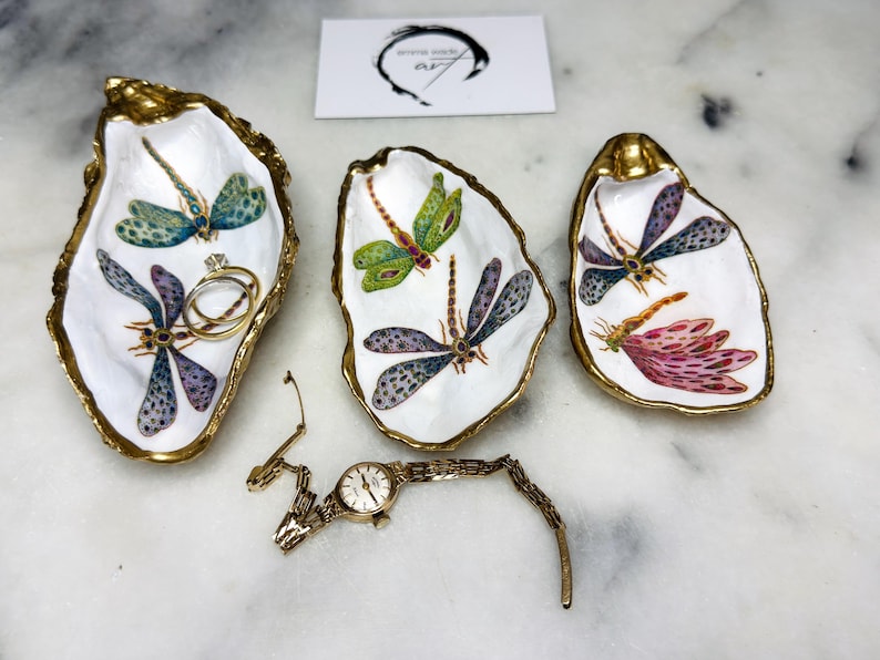 Handmade dragonfly oyster shell trinket dish with hand-gilded gold leaf edges and glossy resin finish, created from sustainably sourced Dorset shells. Unique coastal jewellery holder and ring dish, ideal as a vanity tray, trinket tray or decorative keepsake. Nature inspired home decor gift for birthdays, weddings, anniversaries, housewarmings and Mother’s Day. One of a kind artisan shell dish, beautifully presented in a gift box.