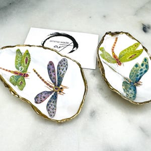 Handmade dragonfly oyster shell trinket dish with hand-gilded gold leaf edges and glossy resin finish, created from sustainably sourced Dorset shells. Unique coastal jewellery holder and ring dish, ideal as a vanity tray, trinket tray or decorative keepsake. Nature inspired home decor gift for birthdays, weddings, anniversaries, housewarmings and Mother’s Day. One of a kind artisan shell dish, beautifully presented in a gift box.