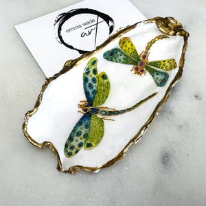 Handmade dragonfly oyster shell trinket dish with hand-gilded gold leaf edges and glossy resin finish, created from sustainably sourced Dorset shells. Unique coastal jewellery holder and ring dish, ideal as a vanity tray, trinket tray or decorative keepsake. Nature inspired home decor gift for birthdays, weddings, anniversaries, housewarmings and Mother’s Day. One of a kind artisan shell dish, beautifully presented in a gift box.