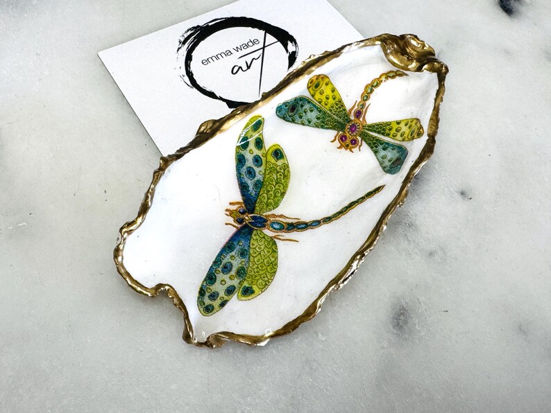 Handmade dragonfly oyster shell trinket dish with hand-gilded gold leaf edges and glossy resin finish, created from sustainably sourced Dorset shells. Unique coastal jewellery holder and ring dish, ideal as a vanity tray, trinket tray or decorative keepsake. Nature inspired home decor gift for birthdays, weddings, anniversaries, housewarmings and Mother’s Day. One of a kind artisan shell dish, beautifully presented in a gift box.