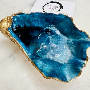 Peut inclure: Un plateau en résine bleu et blanc avec un bord doré, en forme de coquille d'huître.