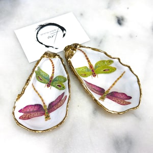 Handmade dragonfly oyster shell trinket dish with hand-gilded gold leaf edges and glossy resin finish, created from sustainably sourced Dorset shells. Unique coastal jewellery holder and ring dish, ideal as a vanity tray, trinket tray or decorative keepsake. Nature inspired home decor gift for birthdays, weddings, anniversaries, housewarmings and Mother’s Day. One of a kind artisan shell dish, beautifully presented in a gift box.