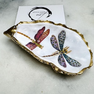 Handmade dragonfly oyster shell trinket dish with hand-gilded gold leaf edges and glossy resin finish, created from sustainably sourced Dorset shells. Unique coastal jewellery holder and ring dish, ideal as a vanity tray, trinket tray or decorative keepsake. Nature inspired home decor gift for birthdays, weddings, anniversaries, housewarmings and Mother’s Day. One of a kind artisan shell dish, beautifully presented in a gift box.