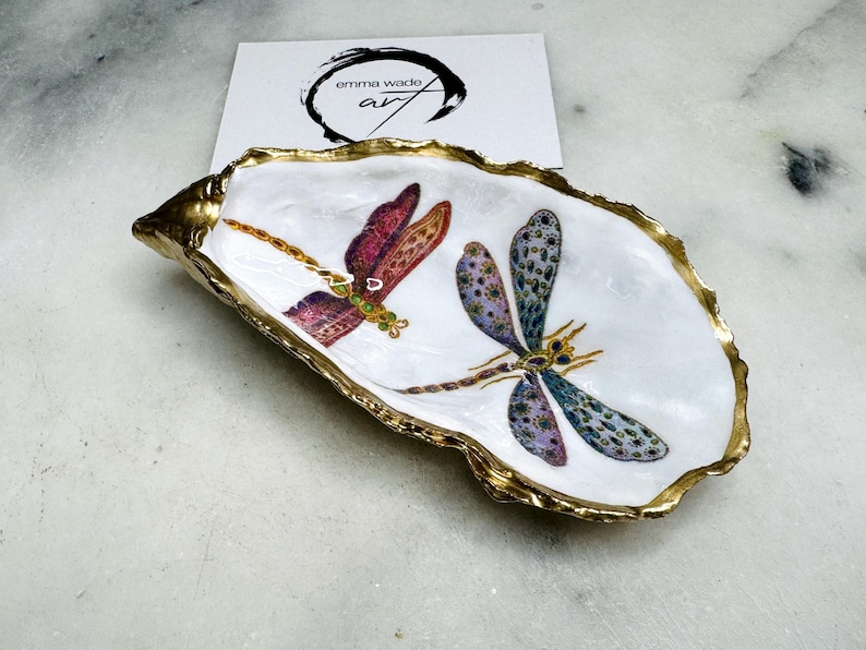 Handmade dragonfly oyster shell trinket dish with hand-gilded gold leaf edges and glossy resin finish, created from sustainably sourced Dorset shells. Unique coastal jewellery holder and ring dish, ideal as a vanity tray, trinket tray or decorative keepsake. Nature inspired home decor gift for birthdays, weddings, anniversaries, housewarmings and Mother’s Day. One of a kind artisan shell dish, beautifully presented in a gift box.