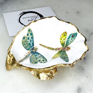 Handmade dragonfly oyster shell trinket dish with hand-gilded gold leaf edges and glossy resin finish, created from sustainably sourced Dorset shells. Unique coastal jewellery holder and ring dish, ideal as a vanity tray, trinket tray or decorative keepsake. Nature inspired home decor gift for birthdays, weddings, anniversaries, housewarmings and Mother’s Day. One of a kind artisan shell dish, beautifully presented in a gift box.