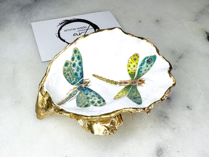 Handmade dragonfly oyster shell trinket dish with hand-gilded gold leaf edges and glossy resin finish, created from sustainably sourced Dorset shells. Unique coastal jewellery holder and ring dish, ideal as a vanity tray, trinket tray or decorative keepsake. Nature inspired home decor gift for birthdays, weddings, anniversaries, housewarmings and Mother’s Day. One of a kind artisan shell dish, beautifully presented in a gift box.