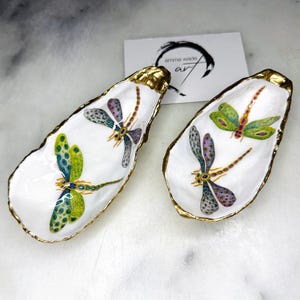 Handmade dragonfly oyster shell trinket dish with hand-gilded gold leaf edges and glossy resin finish, created from sustainably sourced Dorset shells. Unique coastal jewellery holder and ring dish, ideal as a vanity tray, trinket tray or decorative keepsake. Nature inspired home decor gift for birthdays, weddings, anniversaries, housewarmings and Mother’s Day. One of a kind artisan shell dish, beautifully presented in a gift box.
