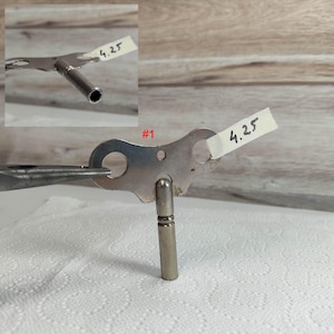 May include: A silver-colored metal key wind-up mechanism with a #1 label and a 4.25 measurement. The key is attached to a metal winding handle with a round hole in the center.