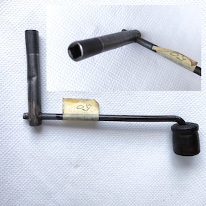 Könnte beinhalten: Ein schwarzer Metallstift mit quadratischem Kopf und abgerundetem Griff. Der Stift hat ein Etikett mit der Nummer "29" darauf.