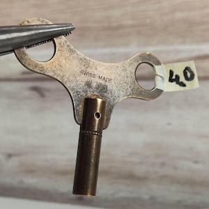 May include: A brass clock winding key with a  'SWISS MADE 400' inscription. The key has a  looped handle and a  square shaft.