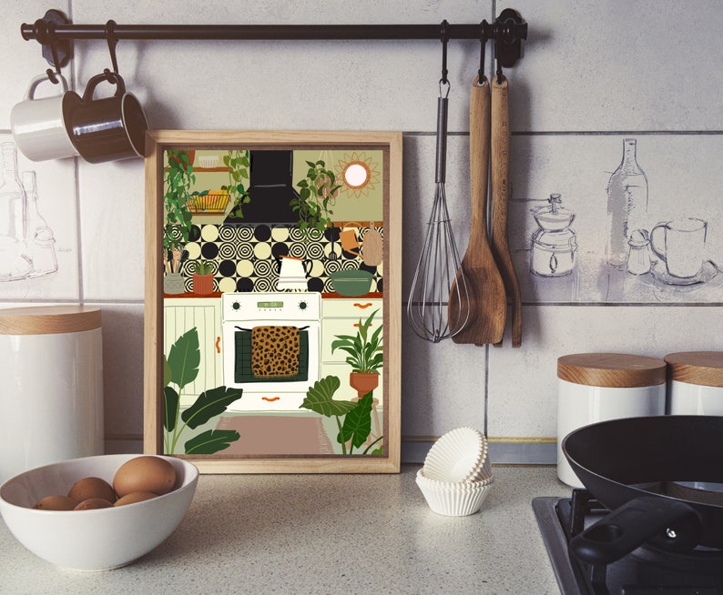 May include: A framed illustration of a kitchen with white cabinets, a black and white tiled backsplash, and a white oven with a leopard print tea towel hanging on the door. The kitchen is decorated with plants and a sun-shaped mirror.