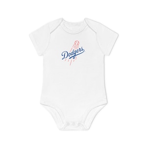 Può includere: Body da bambino bianco con la scritta "Dodgers" in blu, una palla da baseball rossa e linee rosse che si irradiano verso l'esterno. Il body ha maniche corte e bottoni automatici sul fondo.