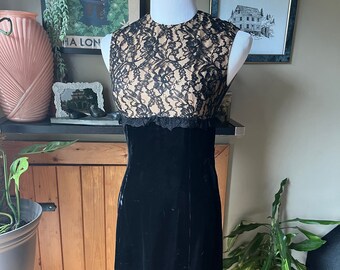 Può includere: Un abito di velluto nero con un corpetto in pizzo. Il pizzo è nero e beige e ha un bordo a festoni. L'abito è senza maniche e ha una silhouette aderente.
