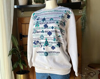 May include: White sweatshirt with a geometric pattern in teal and navy blue. The design includes horizontal stripes and various shapes. The sweatshirt is paired with denim shorts, displayed on a mannequin.