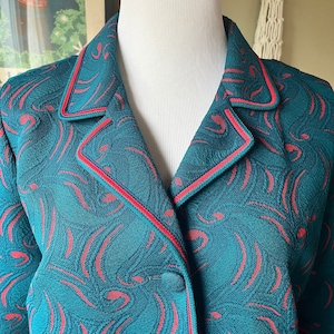 May include: Teal blazer with a red and teal patterned design. The blazer has a notched collar and a single-button closure. The edges are trimmed with red piping. The fabric has a swirling, abstract pattern.