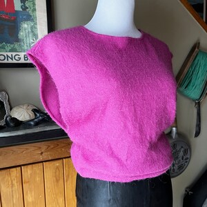 May include: A pink fluffy sleeveless sweater with a round neckline.