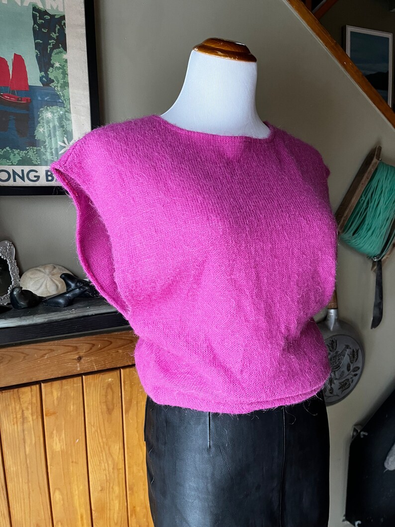 May include: A pink fluffy sleeveless sweater with a round neckline.