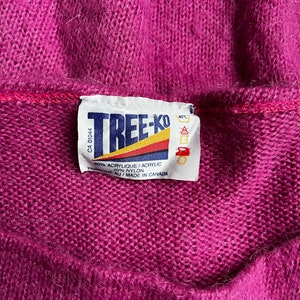 May include: A purple sweater with a white label that reads "TREE-KO" and includes care instructions. The label says "80% Acrylic/Acrylic 20% Nylon" and "Fabrique au/Made in Canada".